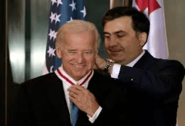A person in a suit shaking another person's hand

Description automatically generated with medium confidence