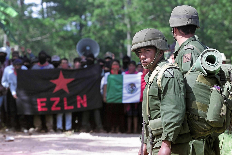 Mexican soldiers stand in front of crowd of protesters holding flags