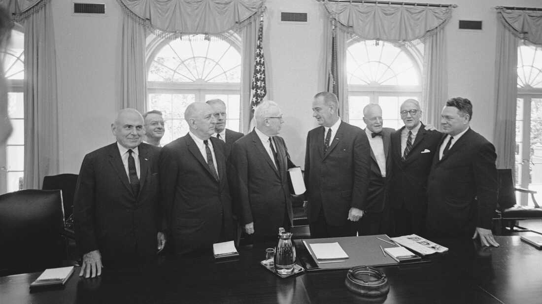 A group of men standing around a table

Description automatically generated with medium confidence