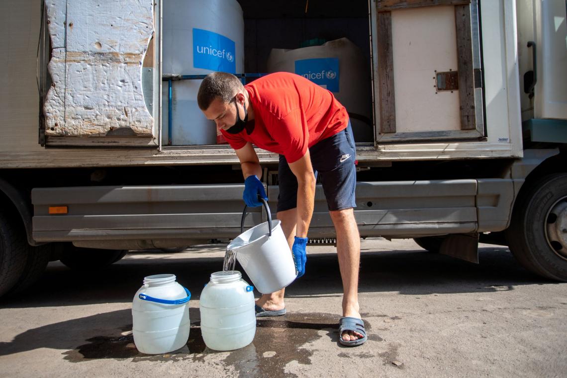 Ukraine. A man fills plastic containers with water.