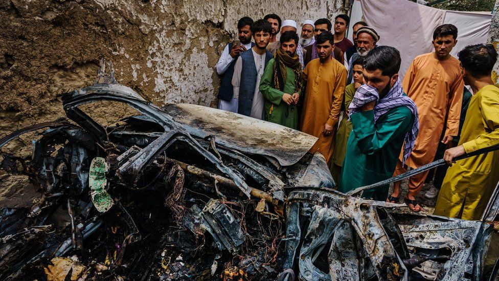 A group of people standing around a car that is badly damaged

Description automatically generated with low confidence