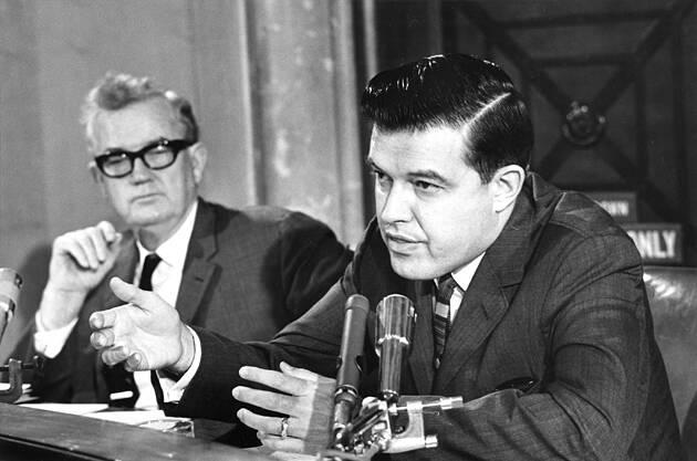 A couple of men sitting at a table with microphones

Description automatically generated with medium confidence