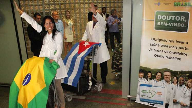 Cuban doctors arrive in Brazil with their two countries' flags draped over luggage trolleys