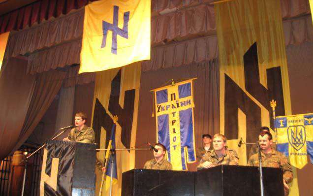 A group of people sitting at a podium with flags in front of them Description automatically generated with low confidence
