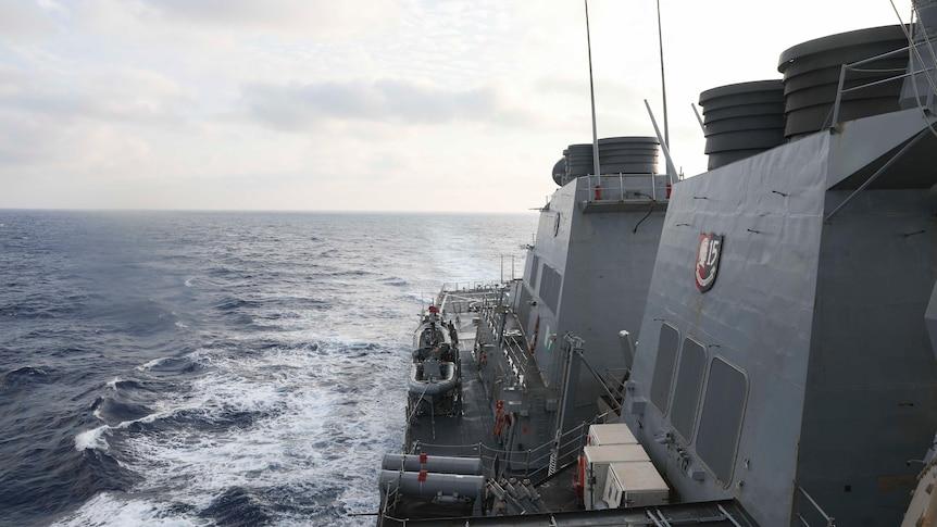 A view of a navy ship with wake left in the ocean visible.