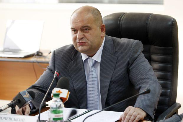 A person in a suit sitting at a desk with microphones

Description automatically generated with medium confidence