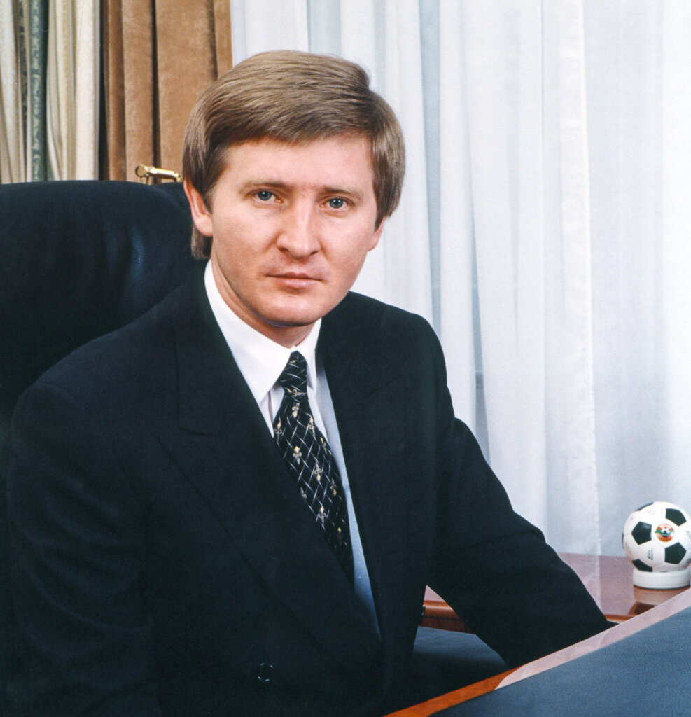 A person in a suit sitting at a desk Description automatically generated with medium confidence