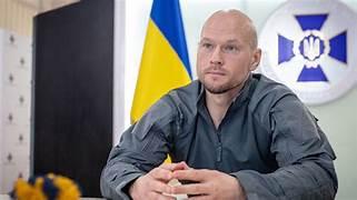 A person sitting at a table with flags behind him

Description automatically generated