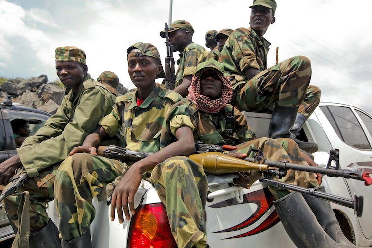 A group of soldiers in camouflage sitting on a back of a truck

Description automatically generated