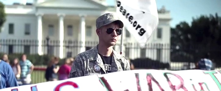 A person in military uniform holding a sign
Description automatically generated