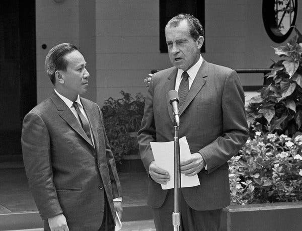 A person in suit standing next to another person in suit
Description automatically generated