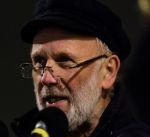 A person with a beard and hat speaking into a microphone
Description automatically generated