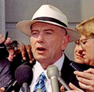 A person in a hat speaking into microphones

Description automatically generated