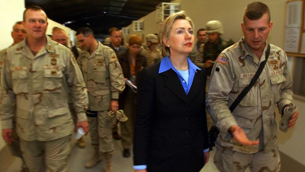 A person in a suit and a person in military uniforms

Description automatically generated
