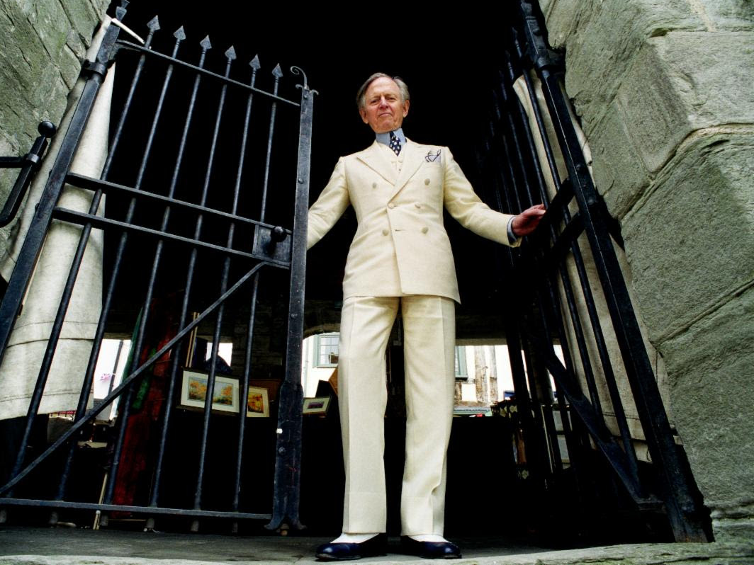 A person in a white suit standing in front of a gate

Description automatically generated