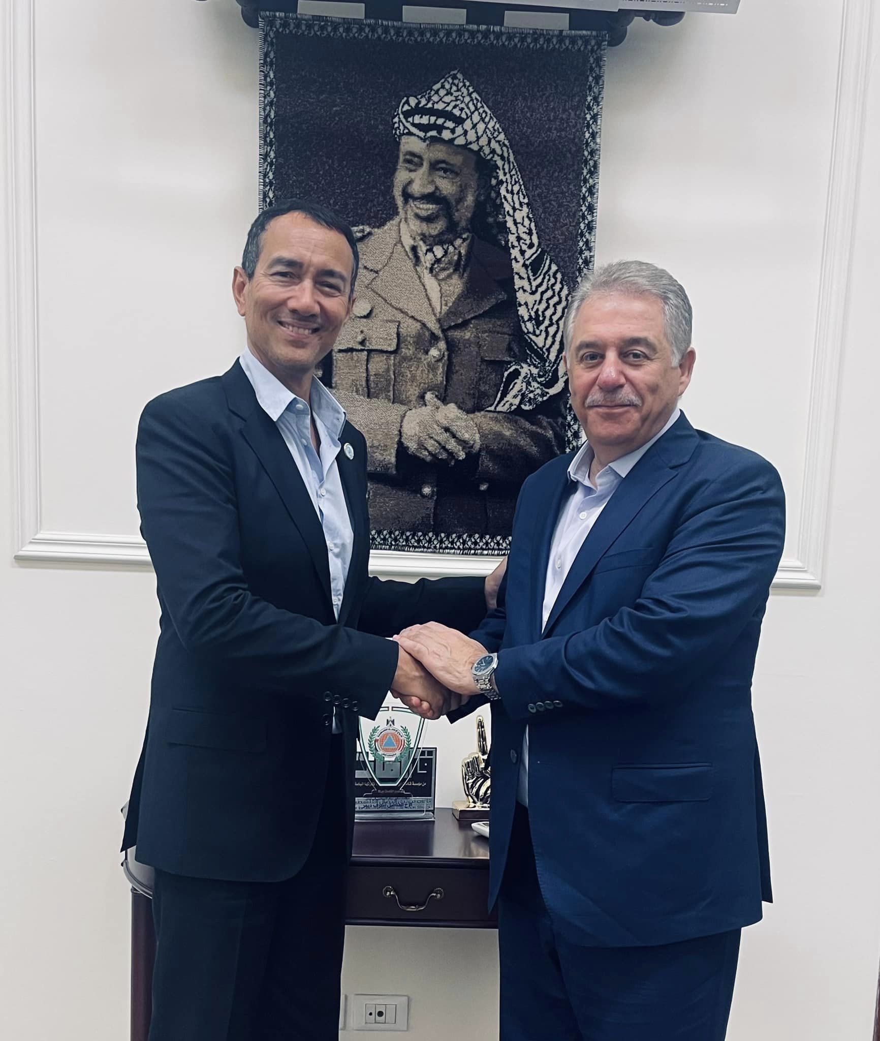 Two men shaking hands in front of a picture

Description automatically generated