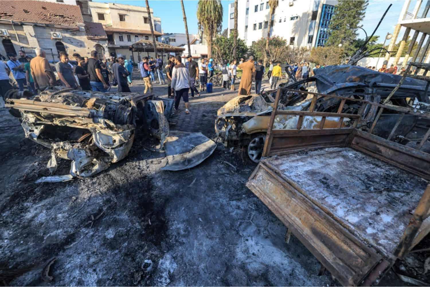 A group of people standing around a burned out car

Description automatically generated