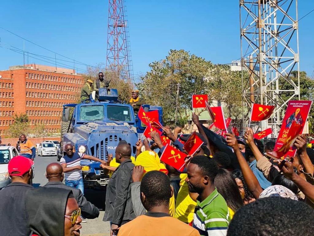 A group of people standing on top of a blue truck
Description automatically generated