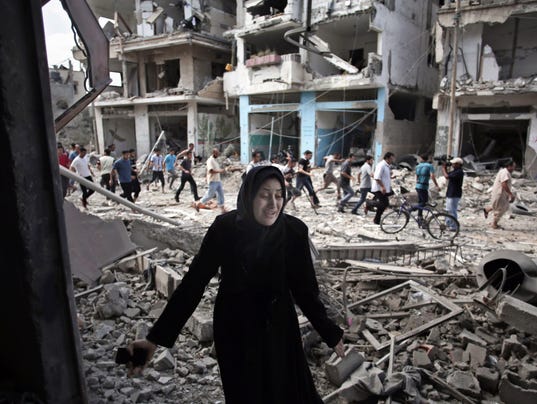 A person in a black robe in front of a destroyed building

Description automatically generated