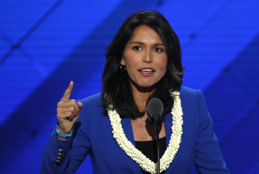 A person in a blue suit pointing at a microphone

Description automatically generated