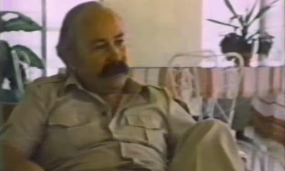 A person with a mustache sitting in a chair

Description automatically generated