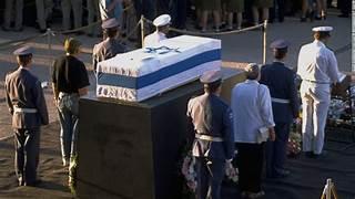 A group of people standing around a coffin
Description automatically generated