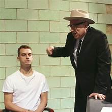 A person in a suit pointing at a person in a white shirt

Description automatically generated