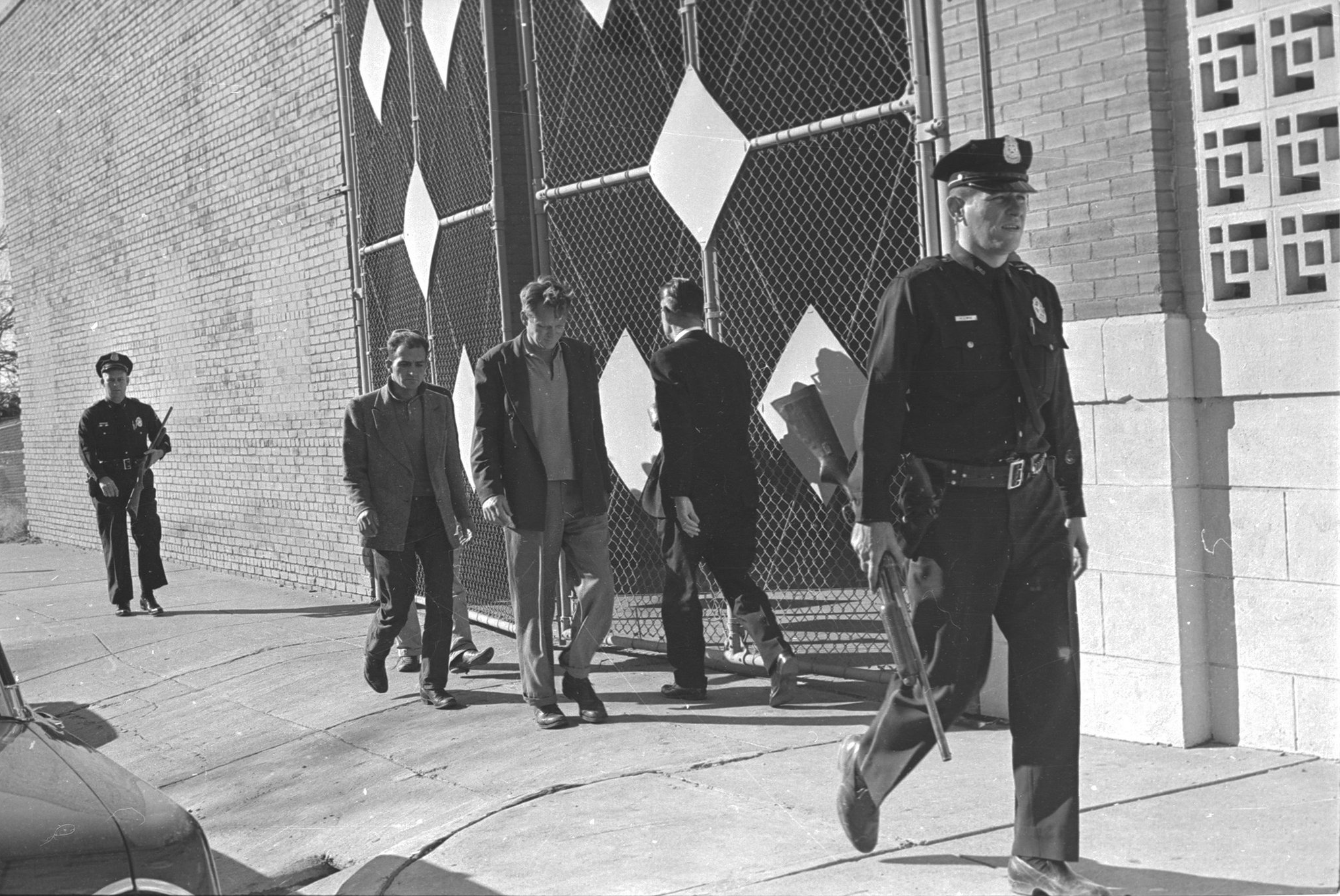 A police officer walking past a group of men

Description automatically generated