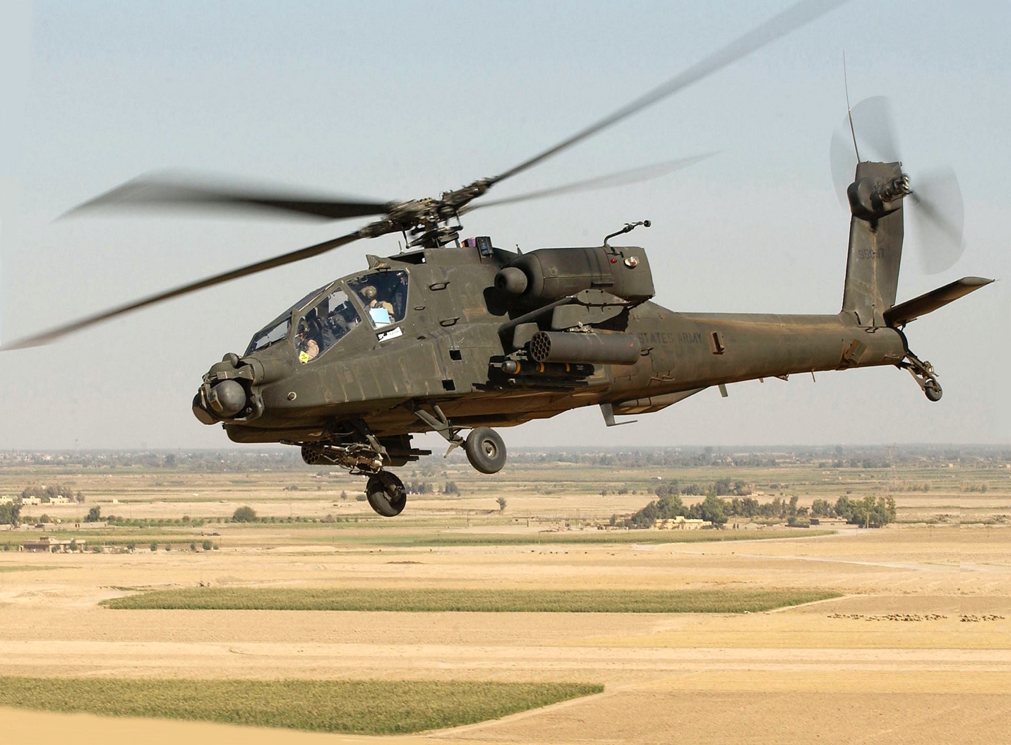 Photo of tilted horizon showing helicopter flying above barren land with rectangular patches of green grass.