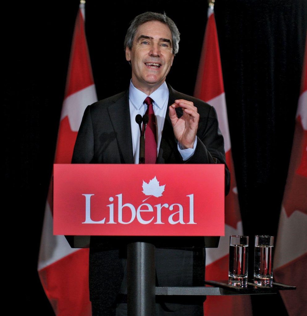 A person standing at a podium with flags behind him

Description automatically generated