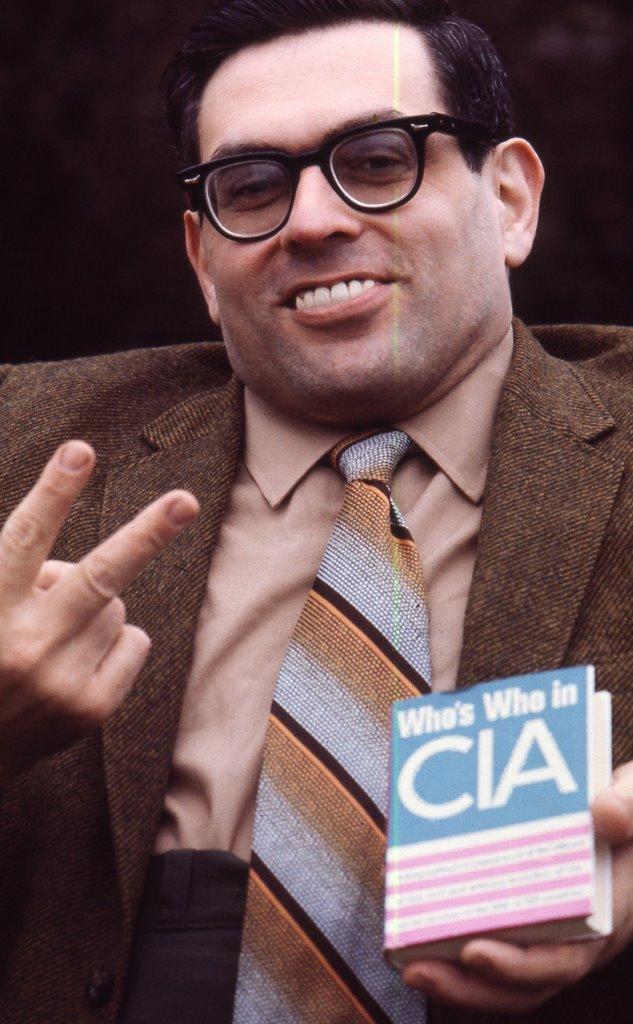 A person wearing glasses and a tie holding up a sign
Description automatically generated