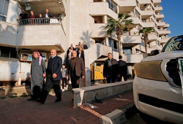 Residents of an apartment building watch from their balconies as a group of men walks past.