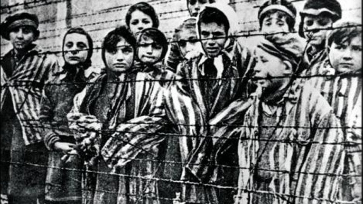 A group of people standing behind a barbed wire fence
Description automatically generated