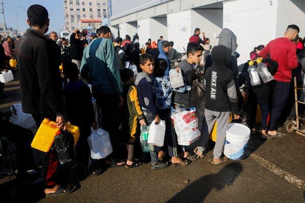 A line of Palestinians, many of them children, carrying large plastic buckets and bottles as they wait in line for drinking water at an outdoor market.