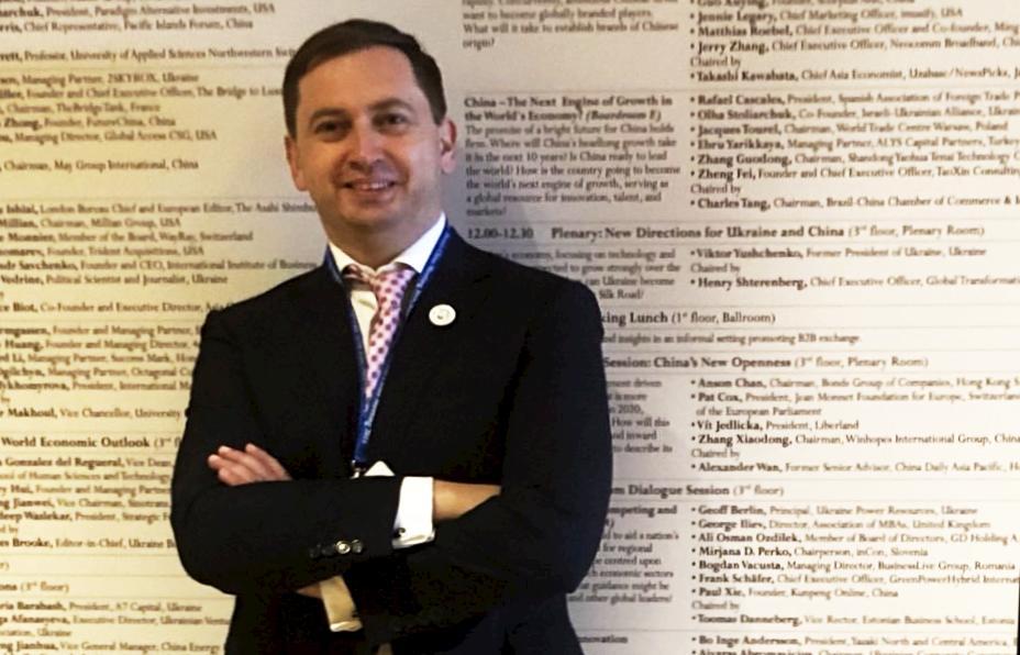 A person in a suit standing in front of a wall with text

Description automatically generated