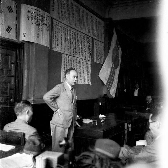 A person standing in front of a desk with a flag
Description automatically generated