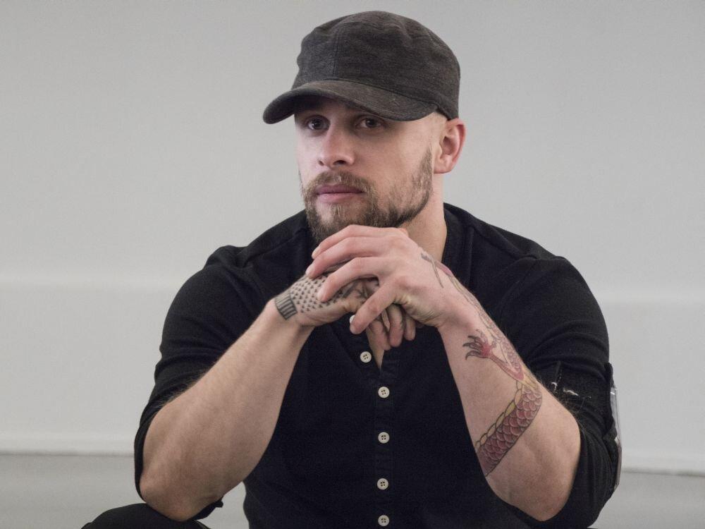 A person with a beard and tattoos on his hands

Description automatically generated