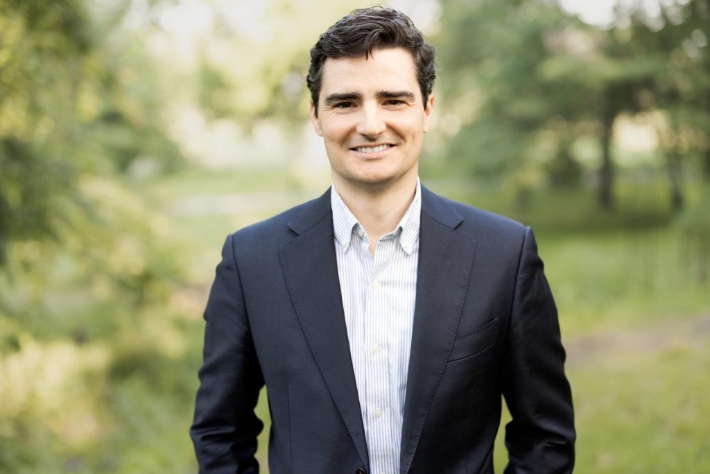 A person in a suit smiling
Description automatically generated