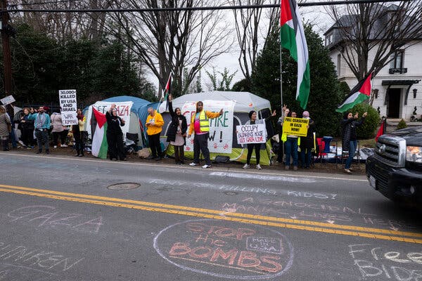 Demonstrators holding signs in support of Gaza. They are standing near a road where chalk drawings.