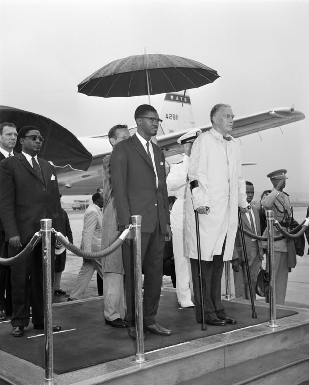 Lumumba, left, of the Republic of the Congo and U.S. Secretary of State Christian Herter stand under an umbrella in the rain