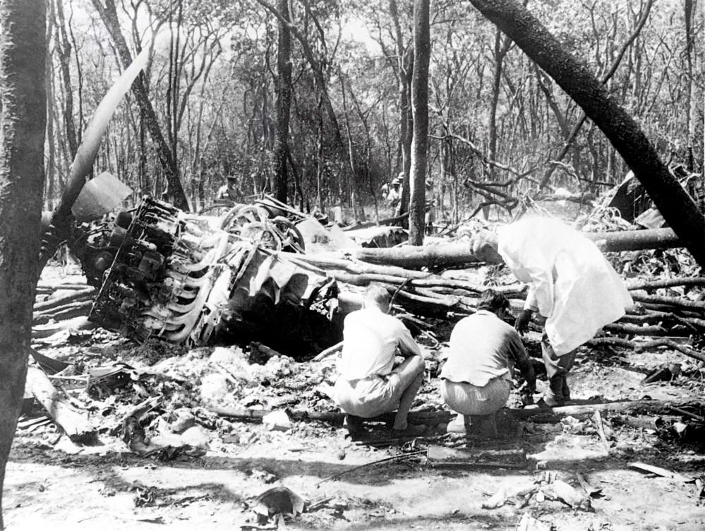 Men working on a plane that crashed into a forest
Description automatically generated