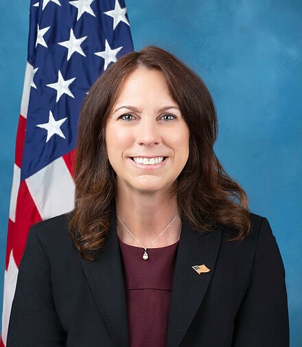 A person smiling in front of a flag

Description automatically generated
