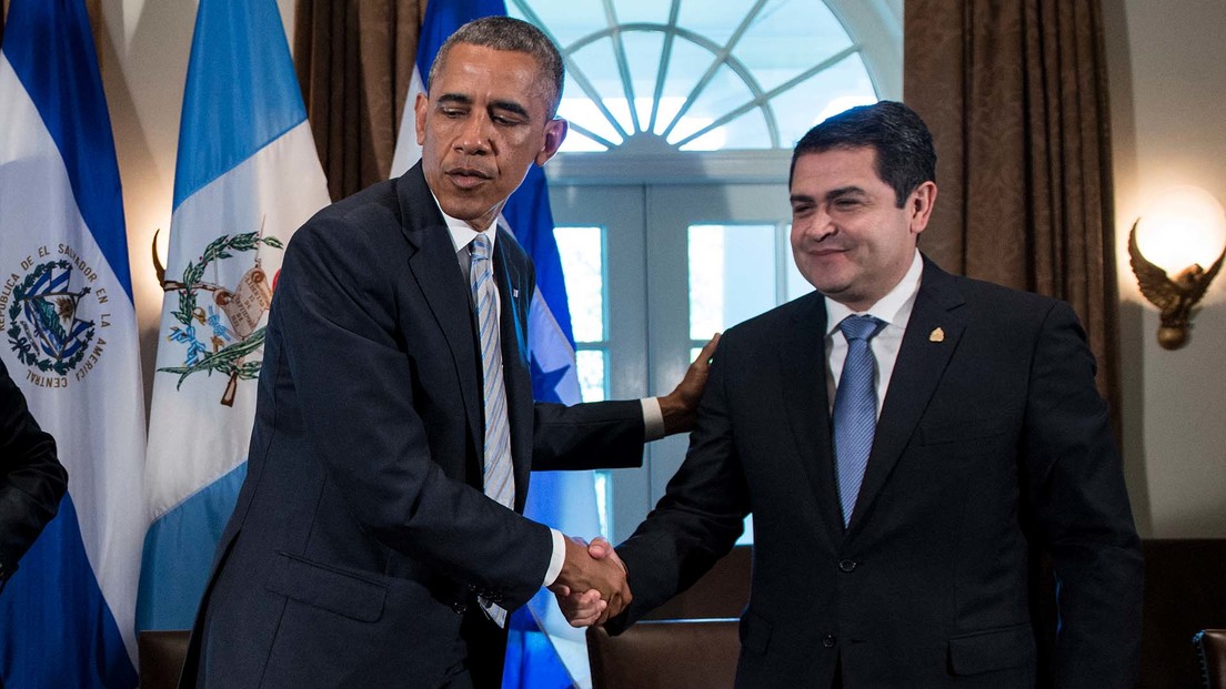 Two men shaking hands in front of flags

Description automatically generated