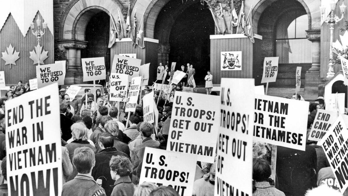 A group of people protesting in front of a building

Description automatically generated
