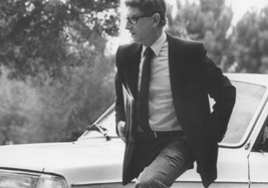 A person in a suit leaning on a car

Description automatically generated