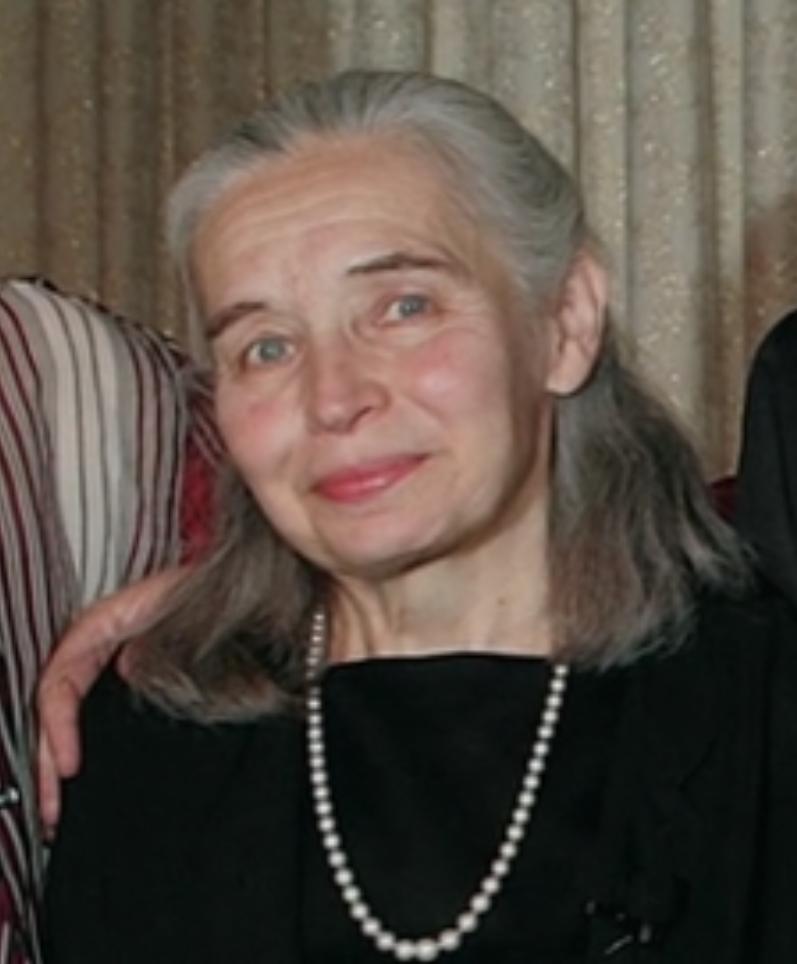 A person with grey hair wearing a pearl necklace

Description automatically generated