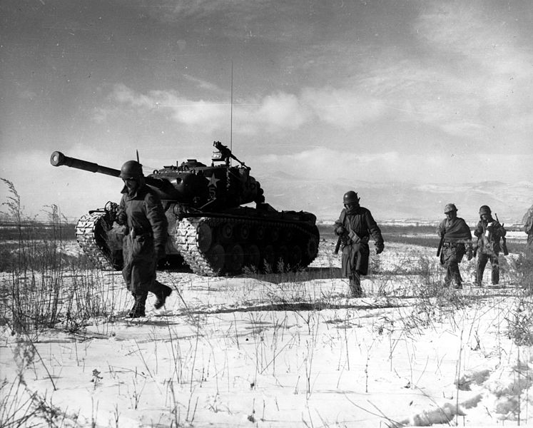 A group of soldiers walking next to a tank

Description automatically generated