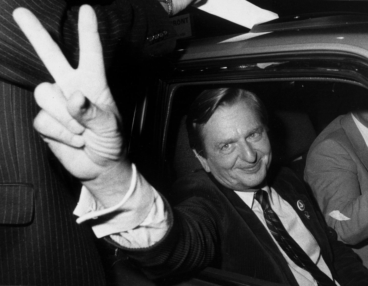 A person in a suit and tie giving a peace sign
Description automatically generated