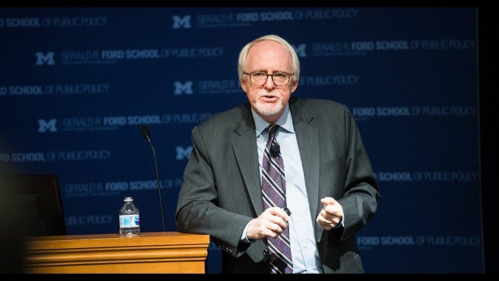A person in a suit standing at a podium

Description automatically generated