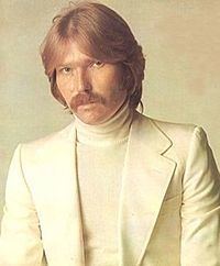 A person with a mustache and a white turtleneck

Description automatically generated